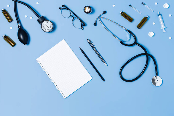 Blauer medizinischer Hintergrund mit verschiedenem Zubehör: Stethoskop, Thermometer, Spritze und Tabletten. - Foto, Bild