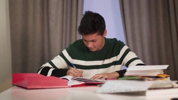 Portrait of smart Asian male student doing homework at the table. Excited teenager making victory gesture and smiling. Education, intelligence, lifestyle, joy. - 映像、動画