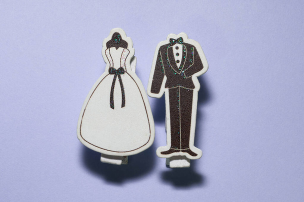 bovenaanzicht van decoratieve lassicistische witte bruiloft en zwarte bruidegom smoking clips samen op paars oppervlak met kopieerruimte, begroeting concept - Foto, afbeelding