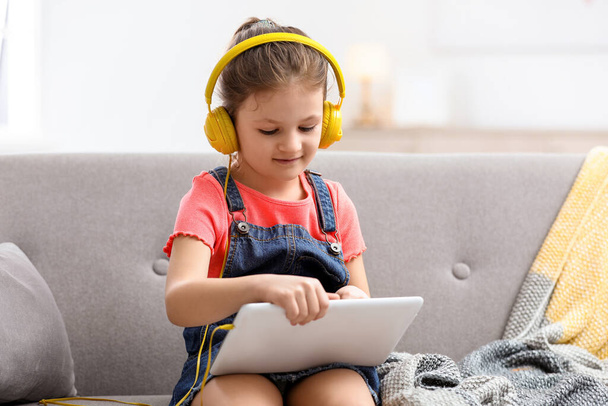 Cute little girl with headphones and tablet on sofa at home - Foto, Bild