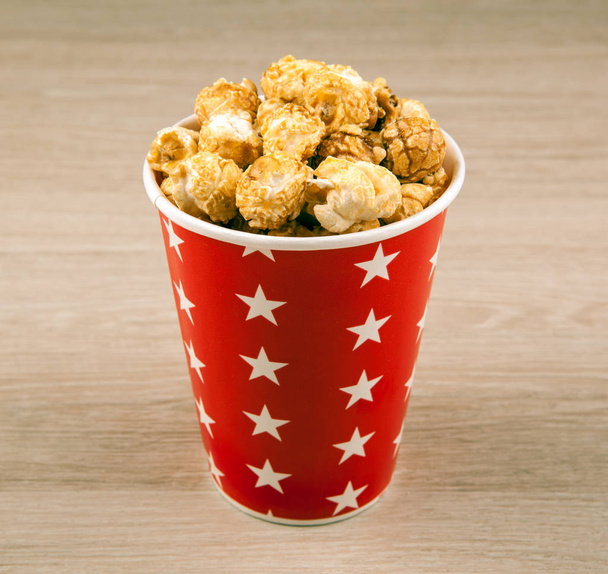 red cardboard cup with sugar popcorn on a wooden table close up - Zdjęcie, obraz