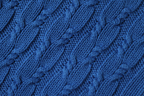 Naadloze gebreide stof met vlechtjes. Gebreide trui, plaid, sjaal. Gebreide achtergrond. Klassieke blauwe kleur 2020 - Foto, afbeelding