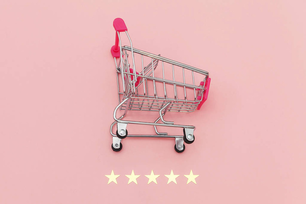 Pequeño supermercado carrito de compras empuje para juguete de compras con ruedas y clasificación de 5 estrellas aislado sobre fondo rosa pastel. Compras al por menor concepto de evaluación y revisión en línea
 - Foto, imagen