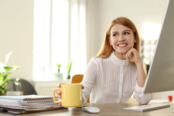 Young woman with cup of drink relaxing at table in office during break - Фото, зображення