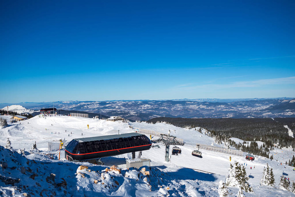 Vue panoramique depuis le sommet de la montagne sur un téléphérique et une piste de ski. La journée est belle et ensoleillée et le ciel est clair et bleu
. - Photo, image