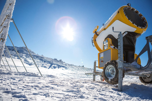 Κίτρινη μηχανή κατασκευής χιονιού στο βουνό κατά τη χειμερινή περίοδο. Είναι μια όμορφη ηλιόλουστη μέρα, όλα είναι καλυμμένα με χιόνι και πίσω είναι ένας καταγάλανος ουρανός. - Φωτογραφία, εικόνα