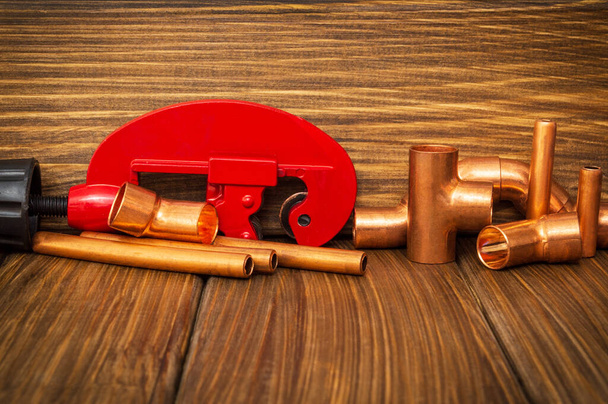 ヴィンテージ木製ボード上のコネクタ付きの赤いパイプカッターと銅パイプ - 写真・画像
