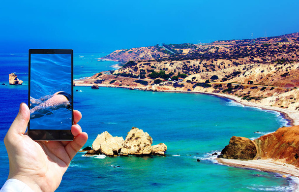 人間の手とスマートフォンを持つアフロディーテの発祥の地近くに青いエメラルド色の海の鮮やかな画像ビキニの女の子 - 写真・画像
