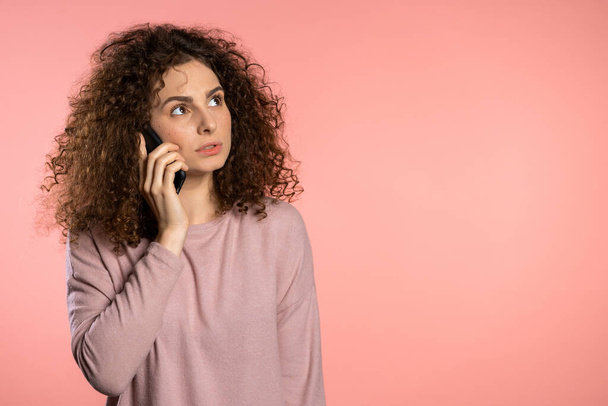 Woman with curly hair talking with somebody by mobile phone. Girl having serious conversation. Technology, mobile connection concept. Copy space - Фото, изображение