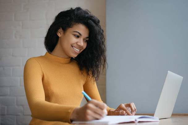 African American student studying, using laptop computer and internet, taking notes on notebook. Online education concept. Young beautiful businesswoman working, planning start up in modern office - Foto, Bild