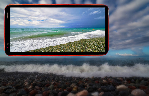 Collage von Handy-Bildschirm auf dunklem mystischem, verschwommenem Hintergrund von welligem Meeresstrand mit nassen Steinen in der Region Sotschi am Schwarzen Meer - Foto, Bild
