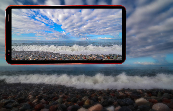 Koláž obrazovky mobilního telefonu na tmavém tajemném rozmazaném pozadí vlnité mořské pláže s mokrými kameny v Soči oblasti Černého moře - Fotografie, Obrázek