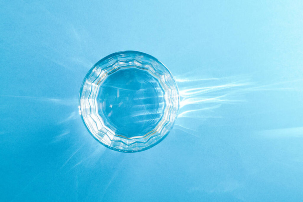 Ein Glas mit klarem, sauberem Wasser steht auf einer blauen Oberfläche. Hartes Licht. Blick von oben. - Foto, Bild
