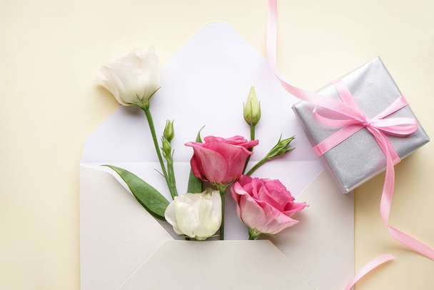 8 de março, Dia Internacional da Mulher. Envelope close-up com eustomas, com uma caixa de presente sobre um fundo amarelo, flat lay
.  - Foto, Imagem