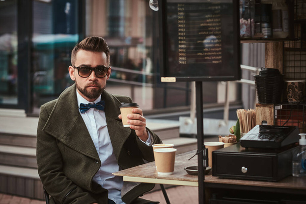 Cliente masculino elegante sentado ao ar livre ao lado de equipamento de tomada de café em um café móvel em uma cidade empório
 - Foto, Imagem