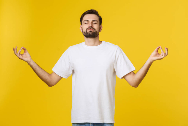 Caucasian young man white t-shirt standing isolated on gray studio background, folding fingers breath exercises process for reducing stress - Zdjęcie, obraz