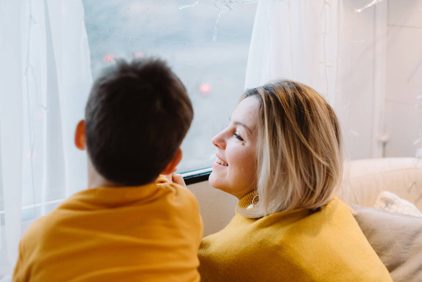 Όμορφη γυναίκα και ο χαριτωμένος γιος της κοιτάζουν έξω από το παράθυρο στο τρέιλερ. Ημέρα της Μητέρας ευχετήρια κάρτα - Φωτογραφία, εικόνα