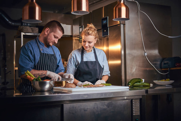 Männlicher Koch mit Assistentin, die in einer Küche steht und in einem Luxusrestaurant Essen zubereitet - Foto, Bild