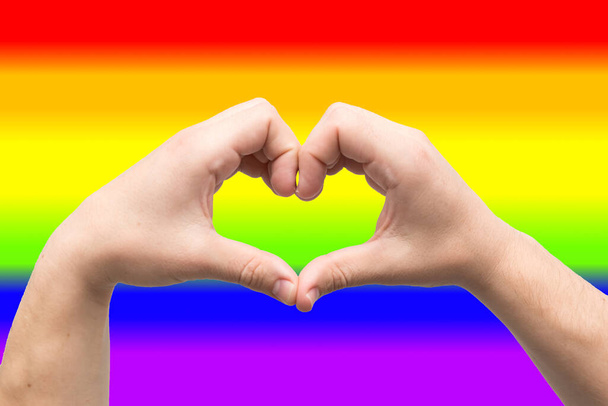 Heart shape made of two male palms isolated on LGBT community color background - Photo, Image