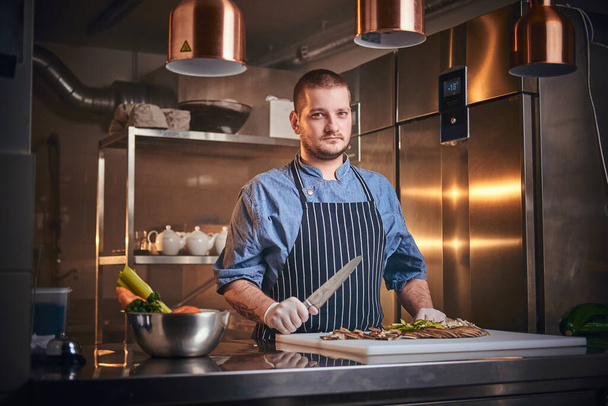 Chef masculino parado en la cocina de un restaurante, sosteniendo un cuchillo
 - Foto, Imagen