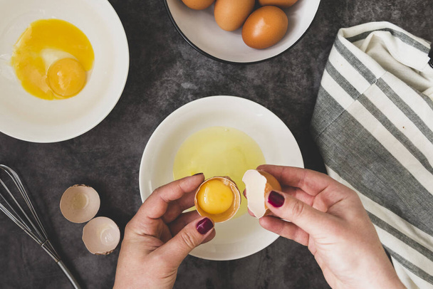 Cooking omlette. Woman's hands cookingomlette, breaking an fresh egg. Dark background, food flat lay - Photo, Image