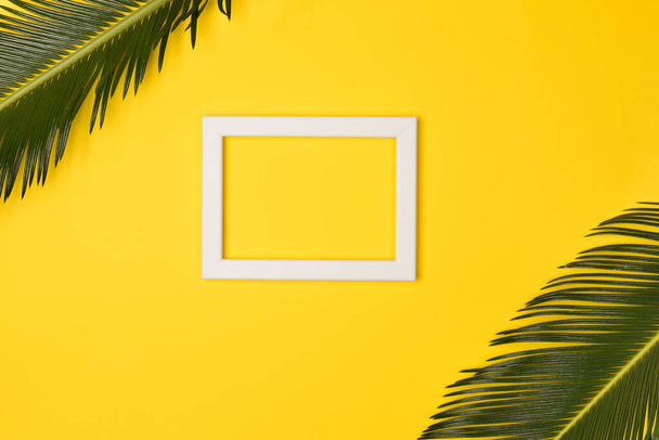 Palm leaves and photo frame, on yellow background. Top view, copy space. Flat lay. - Photo, Image