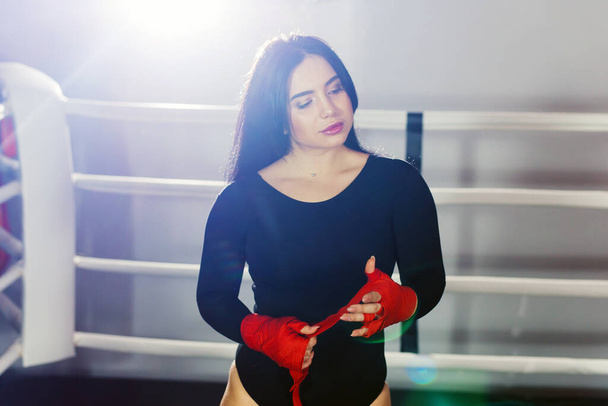 Mujer sexy está envolviendo las manos con envolturas de boxeo rojo. Una chica en un cuerpo negro envuelve las manos con vendas. El concepto de feminismo y disposición a luchar
 - Foto, Imagen