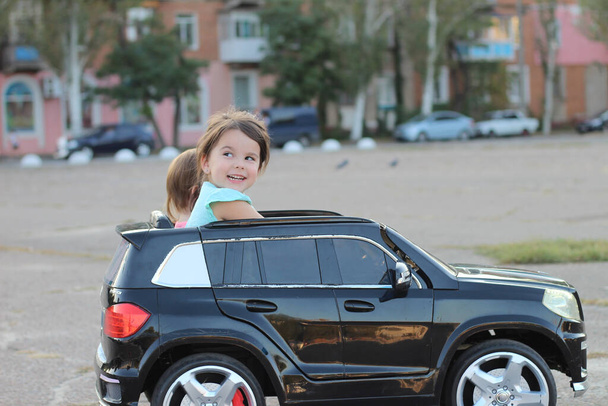 Duas garotas incríveis montam em um grande carro de brinquedo no asfalto da rua da cidade. Dirigir ao ar livre em uma atração de verão para crianças
 - Foto, Imagem