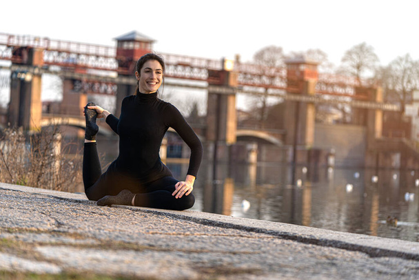 Πορτρέτο του αθλητικού κοριτσιού που κάνει γιόγκα τεντώνοντας άσκηση στην όχθη του ποταμού - Φωτογραφία, εικόνα