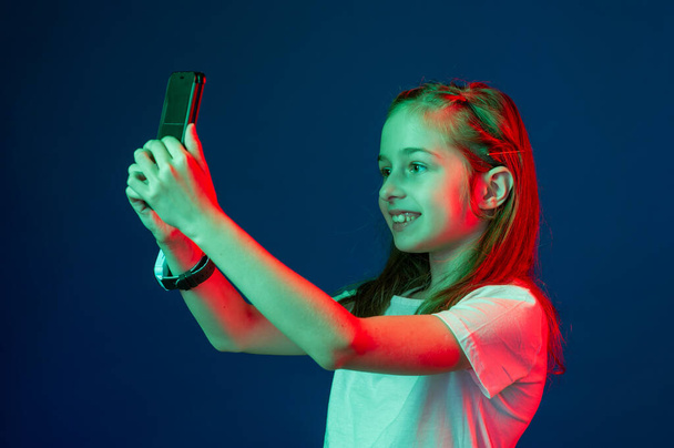 Nastolatek rozmawiający przez smartfona. Dziewczyna ze smartfonem w rękach. Dziewczyna ze smartfonem w rękach czerwonego zielonego filtra. Smartwatch 9-letnia dziewczynka fotografuje się przez telefon - Zdjęcie, obraz