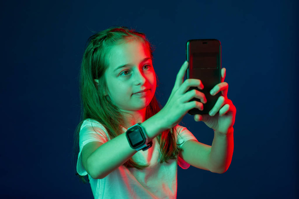 Nastolatek rozmawiający przez smartfona. Dziewczyna ze smartfonem w rękach. Dziewczyna ze smartfonem w rękach czerwonego zielonego filtra. Smartwatch 9-letnia dziewczynka fotografuje się przez telefon - Zdjęcie, obraz