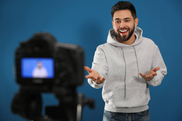 Young blogger recording video on camera against blue background - Foto, Imagem