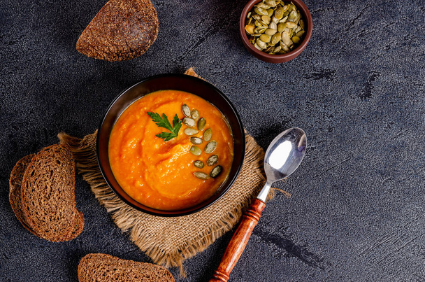 Vegetarian autumn cream soup of pumpkins and carrots with seeds and parsley on a dark background with copy space, flat lay. Healthy eating concept. Horizontal orientation. View from above. - Foto, Bild