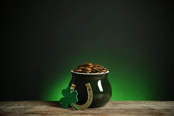 Pot with gold coins, horseshoe and clover on wooden table against dark background. St. Patrick's Day celebration - Foto, afbeelding