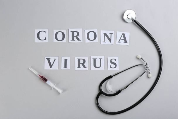 Flat lay composition with words CORONA VIRUS, stethoscope and syringe on light grey background - Valokuva, kuva