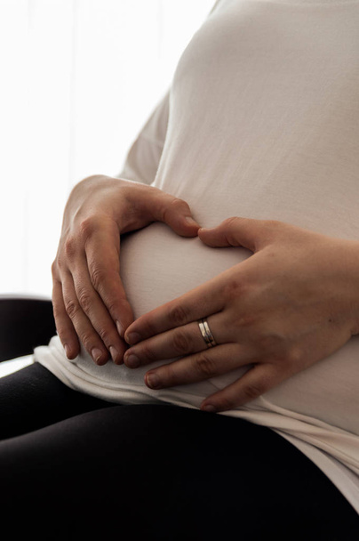 Schwangere 30-Jährige mit herzförmigen Händen am Schwangerschaftsbauch - Foto, Bild