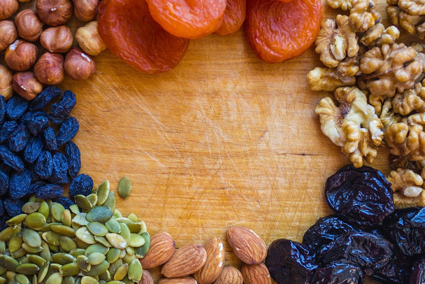 Organic food, a natural source of protein, vitamins, minerals. Nuts, dried apricots, raisins, prunes and pumpkin seeds on an old wooden board. Daylight. - Photo, Image