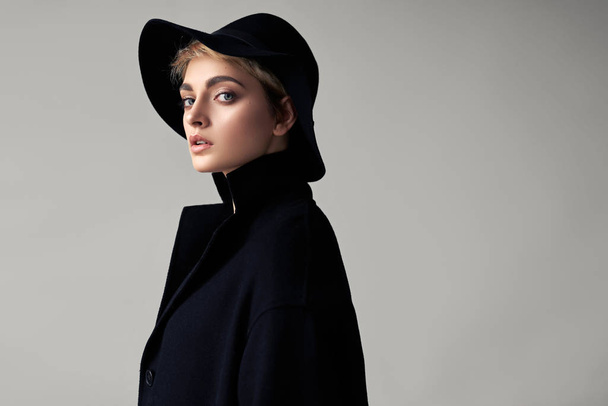 Portrait of beautiful model in stylish black hat and coat isolated on gray background - 写真・画像