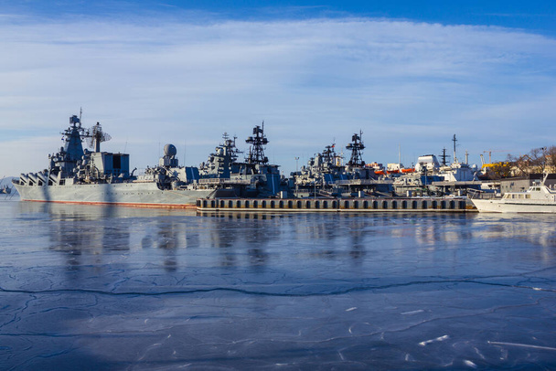 Gri gemiler, şehrin kıyısına yakın bir askeri filo. Donanma, üssün yeri. Soğuk hava, deniz buzla kaplı. Baharın başında. Güneş ışığı. - Fotoğraf, Görsel