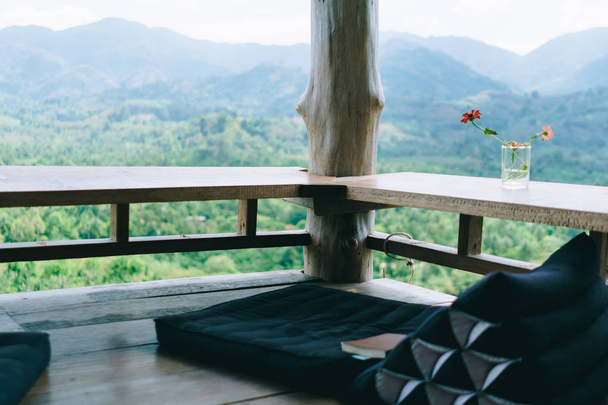 木製のテーブルと緑の自然木の山の景色の背景と周りのヴィンテージタイスタイルの床席。リラックスする家の美しいテラス. - 写真・画像
