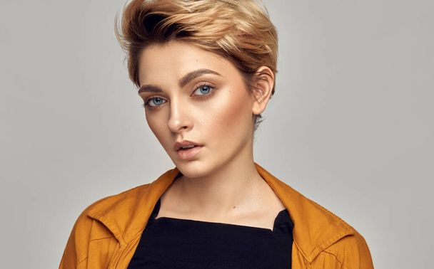 Close up face of young female model with blue eyes and short blonde hair isolated on gray background - 写真・画像