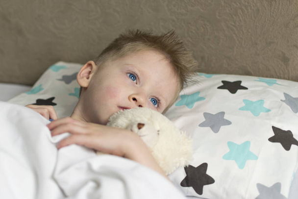 A criança triste doente na temperatura está na cama com um urso de brinquedo. Gripe constipações vírus da doença bacterium
 - Foto, Imagem