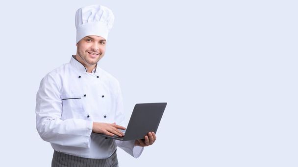 Веселый шеф-повар с ноутбуком Просмотр Интернет, стоящий в студии, Панорама
 - Фото, изображение