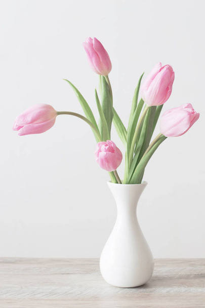 pink tulips in white ceramic vase on wooden table on background white wall - Photo, Image