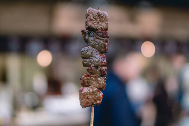 A hand holding a grilled meat on a skewer - Photo, Image