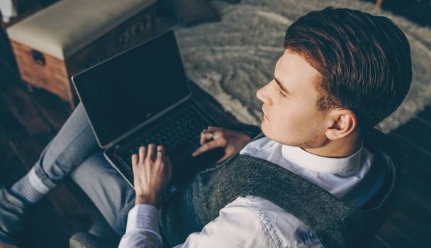 Vestidos formales chico caucásico sentado en un sofá y sosteniendo una PC mientras piensa en planes de negocios futuros
 - Foto, Imagen