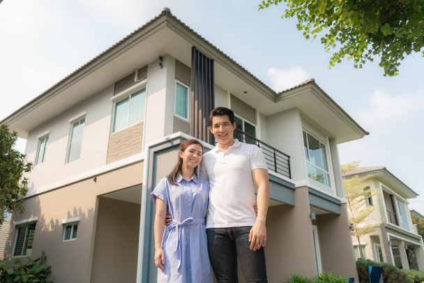 Retrato de una joven pareja asiática de pie y abrazándose juntos luciendo felices frente a su nueva casa para comenzar una nueva vida. Familia, edad, hogar, bienes raíces y concepto de personas - Foto, imagen