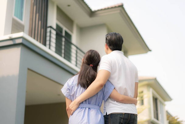 Voltar retrato do jovem casal asiático de pé e abraçando juntos olhando feliz na frente de sua nova casa para começar uma nova vida. Família, idade, casa, imobiliário e conceito de pessoas - Foto, Imagem