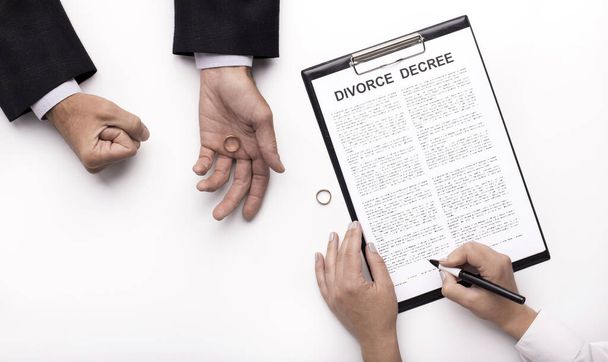 Husband holding wedding ring while wife signing divorce decree - Foto, Bild