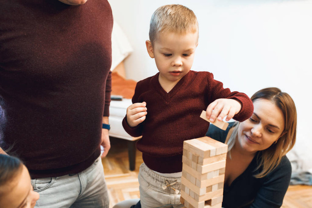 Caucasian parents playing jenga with their son being dressed in red sweater and white jeans - Photo, Image